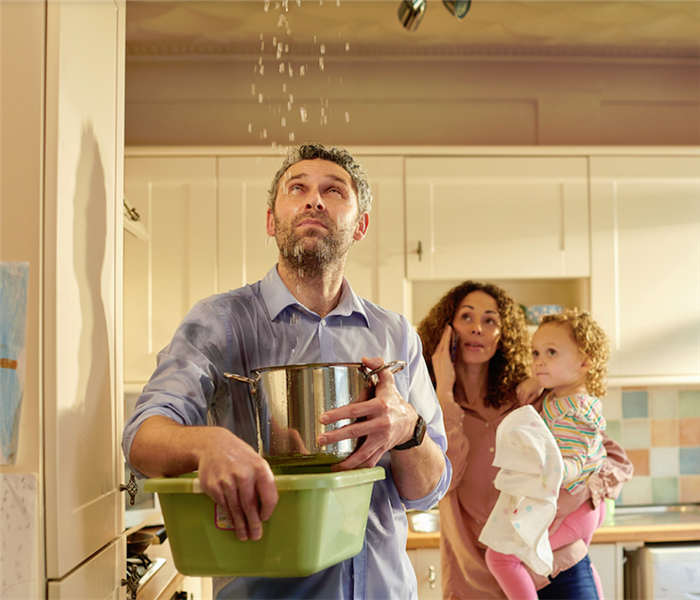 a man holding pots to catch water falling from his ceiling